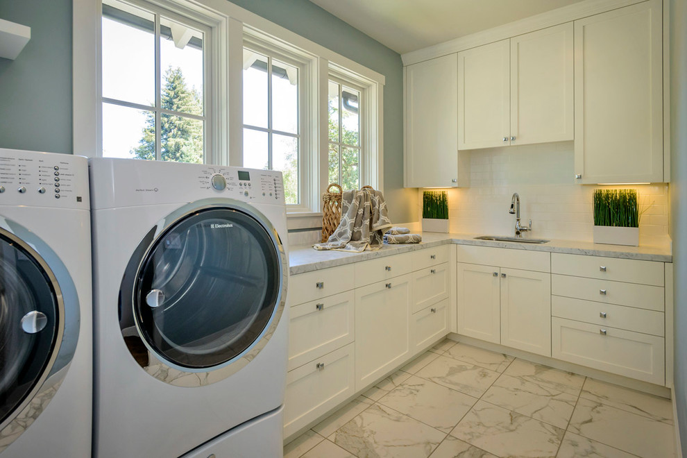 Diseño de lavadero en L tradicional renovado con fregadero bajoencimera, armarios estilo shaker, puertas de armario blancas, lavadora y secadora juntas y encimeras grises