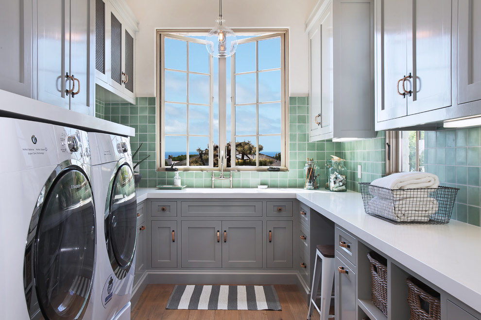 Immagine di una sala lavanderia mediterranea con ante in stile shaker, ante grigie, lavatrice e asciugatrice affiancate, pavimento marrone e top bianco