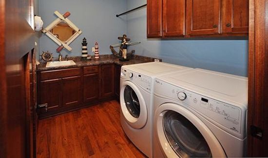 Imagen de cuarto de lavado en L pequeño con fregadero encastrado, armarios estilo shaker, puertas de armario de madera oscura, paredes azules, suelo de madera en tonos medios y lavadora y secadora juntas