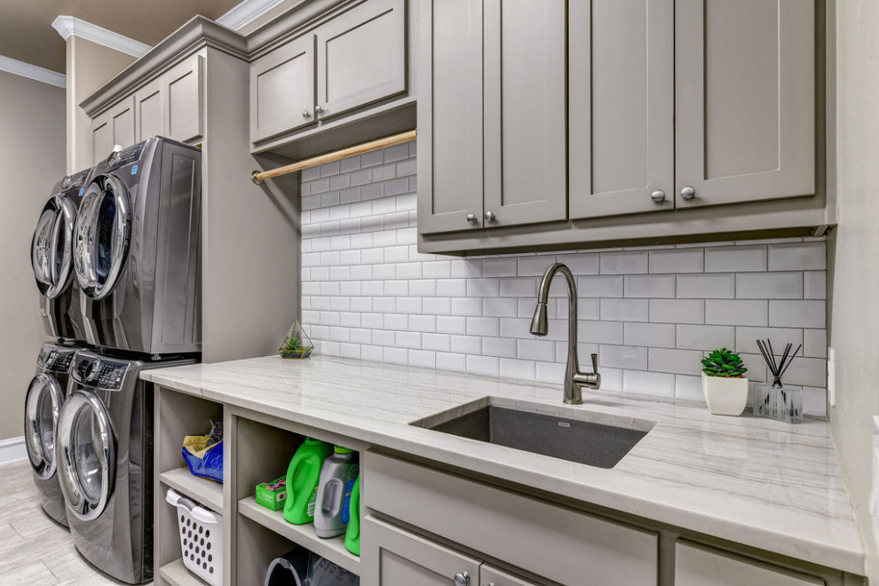 This is an example of an expansive traditional single-wall utility room in Dallas with a submerged sink, shaker cabinets, grey cabinets, quartz worktops, grey walls, porcelain flooring, a stacked washer and dryer, white floors and grey worktops.