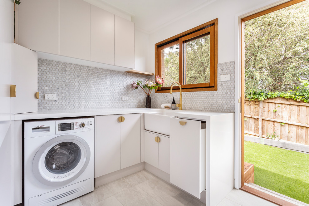 Moderne Waschküche in L-Form mit Waschmaschine und Trockner integriert, Landhausspüle, flächenbündigen Schrankfronten, weißen Schränken, weißer Wandfarbe, beigem Boden und weißer Arbeitsplatte in Melbourne