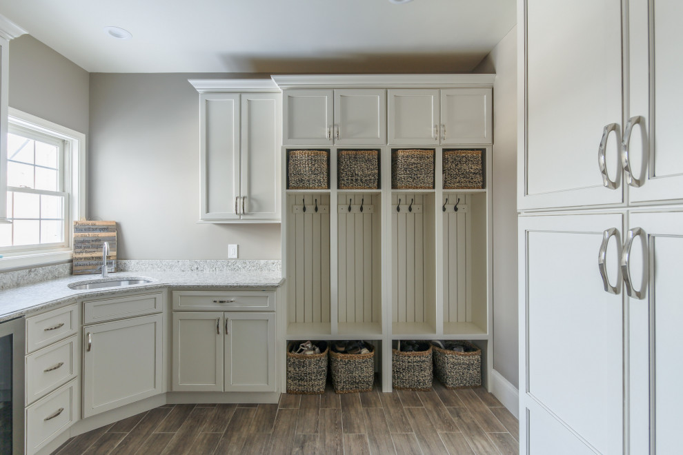 Inspiration for a mid-sized transitional l-shaped dark wood floor and brown floor dedicated laundry room remodel in Detroit with an undermount sink, recessed-panel cabinets, white cabinets, quartz countertops, gray walls, a stacked washer/dryer and white countertops