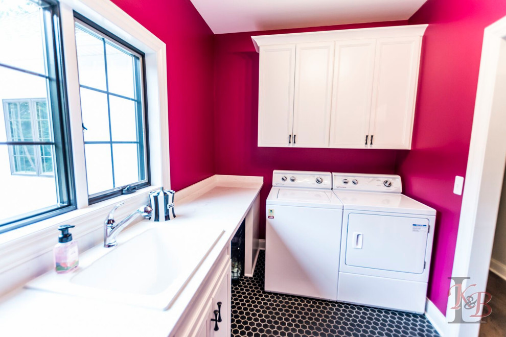 Cette image montre une buanderie parallèle dédiée avec un évier utilitaire, un placard avec porte à panneau encastré, un mur rose, un sol en carrelage de céramique, des machines côte à côte, un sol noir et un plan de travail blanc.