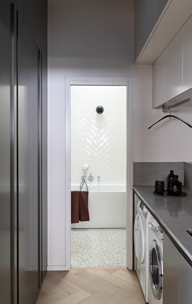 This is an example of a contemporary l-shaped utility room in Melbourne with a submerged sink, flat-panel cabinets, white cabinets, light hardwood flooring, beige floors and white worktops.