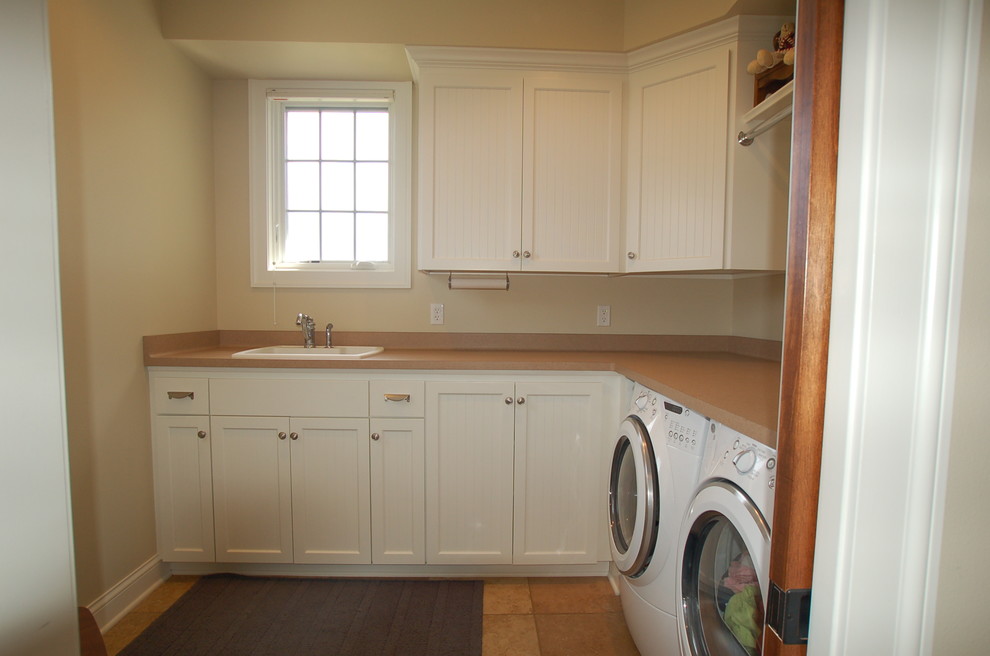 Bild på en mellanstor funkis l-formad tvättstuga, med en enkel diskho, vita skåp, laminatbänkskiva, beige väggar, klinkergolv i keramik, en tvättmaskin och torktumlare bredvid varandra och luckor med infälld panel