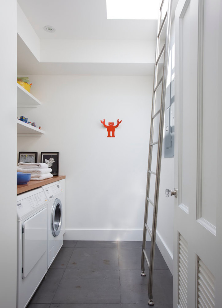 Mid-sized transitional galley dedicated laundry room photo in New York with flat-panel cabinets, white cabinets, wood countertops, white walls and a side-by-side washer/dryer