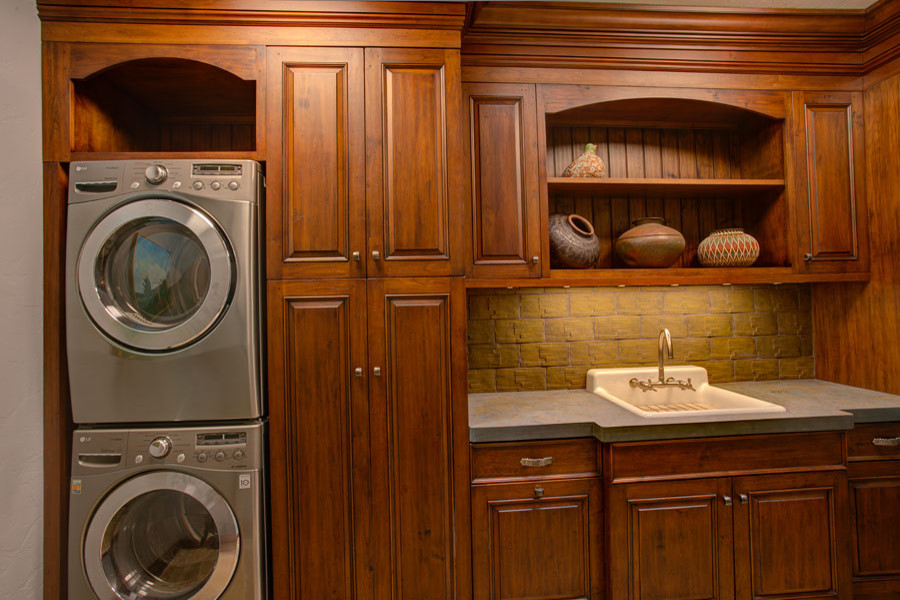 Diseño de lavadero tradicional con armarios con paneles con relieve, puertas de armario de madera oscura y lavadora y secadora apiladas