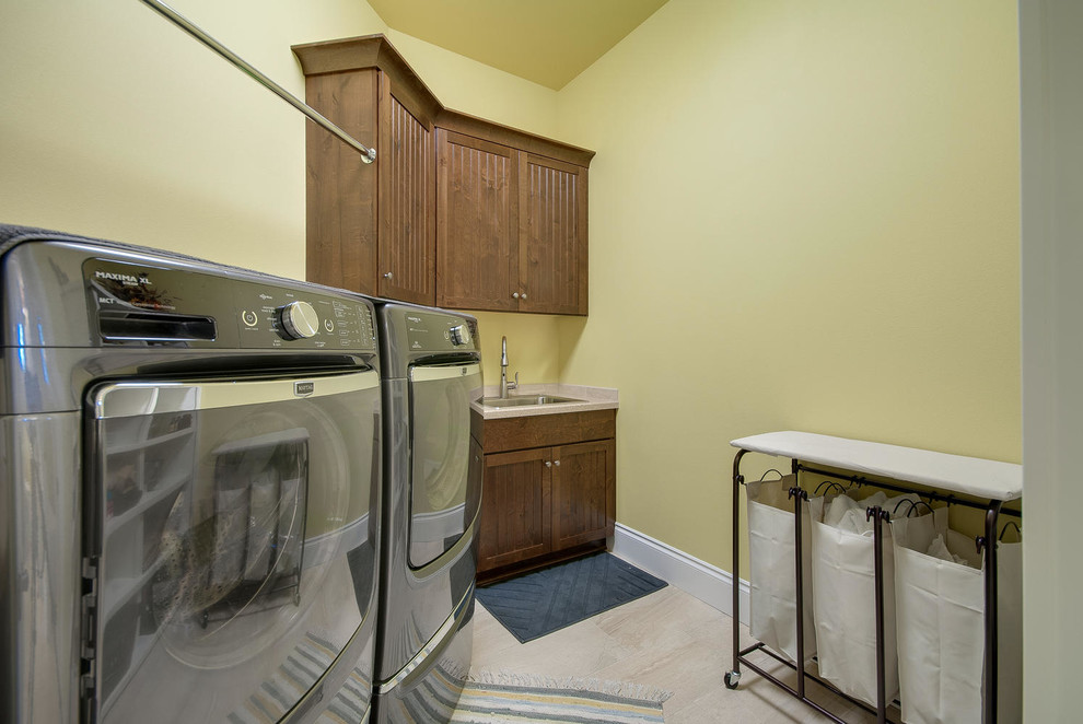 Bild på en liten amerikansk tvättstuga enbart för tvätt, med en nedsänkt diskho, gula väggar och en tvättmaskin och torktumlare bredvid varandra