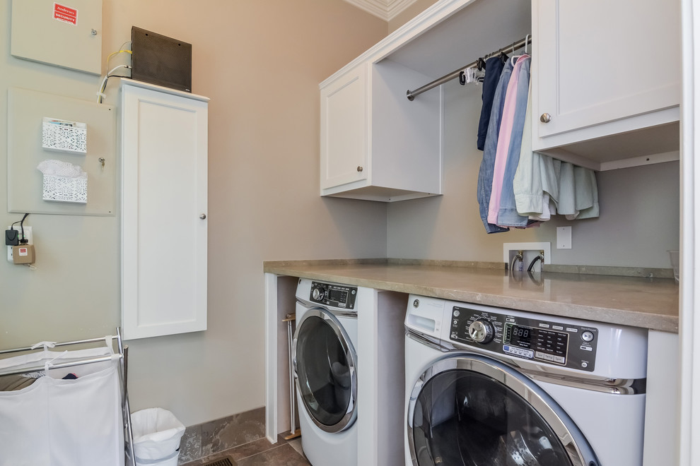 Imagen de lavadero lineal clásico de tamaño medio con puertas de armario blancas, paredes beige, suelo de baldosas de cerámica y lavadora y secadora juntas