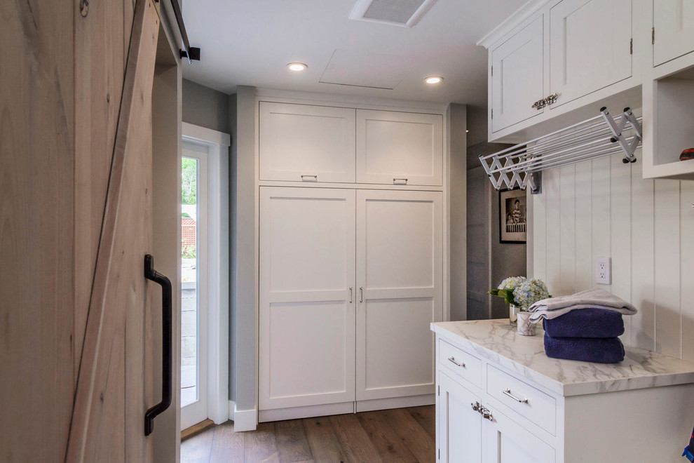 Photo of a large traditional galley utility room in San Francisco with shaker cabinets, white cabinets, grey walls, dark hardwood flooring and a concealed washer and dryer.