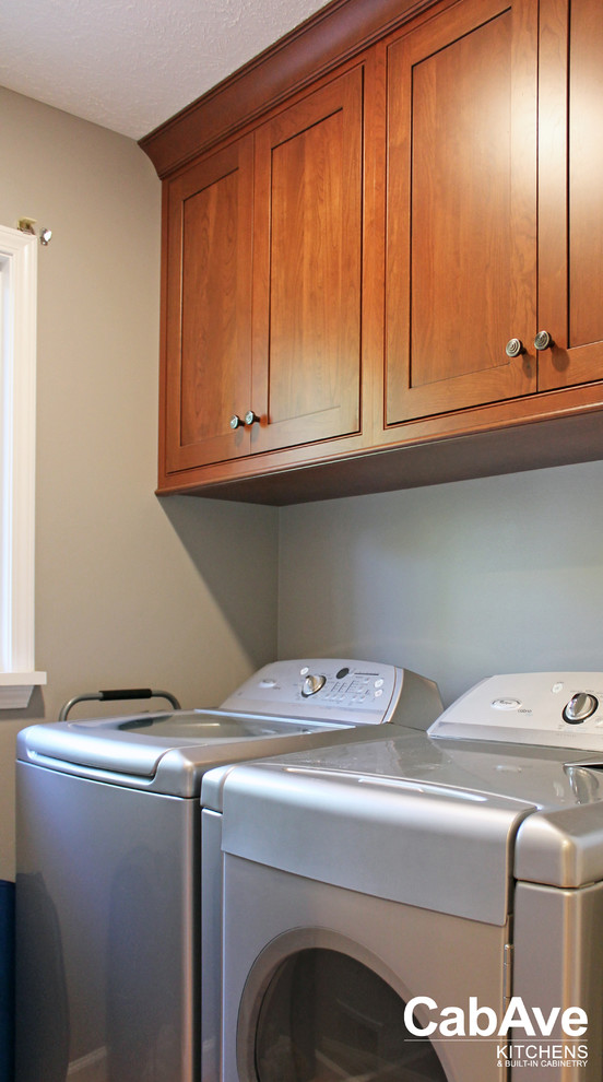 Small transitional single-wall medium tone wood floor and brown floor dedicated laundry room photo in Other with beaded inset cabinets, medium tone wood cabinets, gray walls and a side-by-side washer/dryer