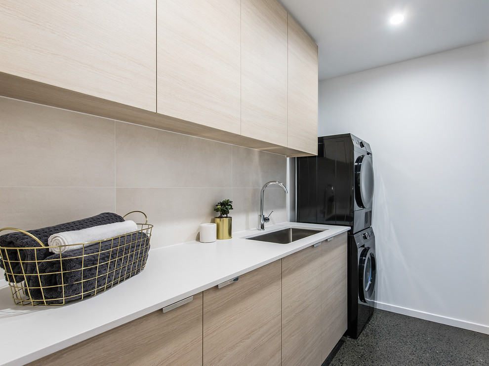 ブリスベンにあるコンテンポラリースタイルのおしゃれな洗濯室 (アンダーカウンターシンク、フラットパネル扉のキャビネット、白い壁、上下配置の洗濯機・乾燥機、グレーの床、淡色木目調キャビネット) の写真