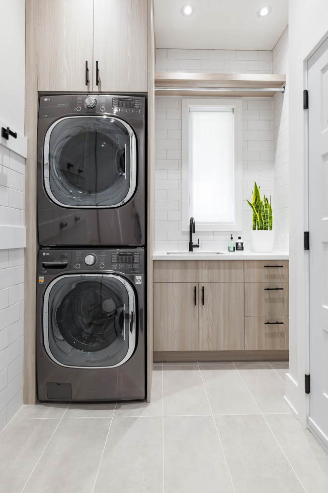Photo of a small contemporary u-shaped separated utility room in Toronto with a submerged sink, flat-panel cabinets, beige cabinets, quartz worktops, white walls, ceramic flooring, a stacked washer and dryer, grey floors and white worktops.