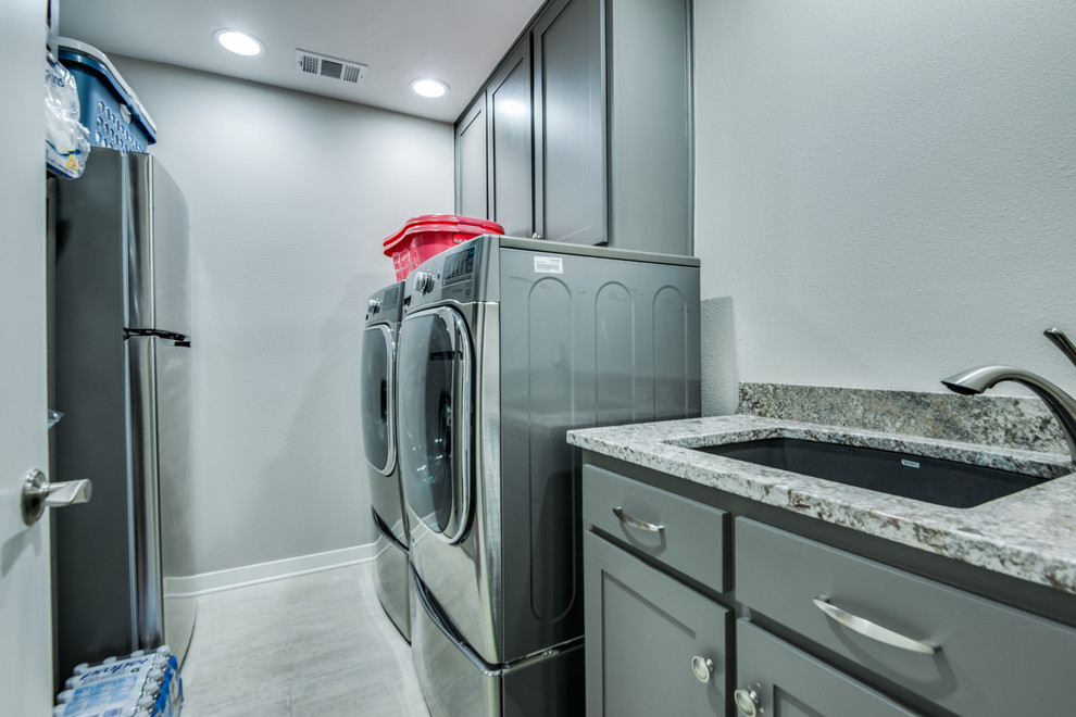 Example of a small transitional galley porcelain tile and gray floor utility room design in Dallas with an undermount sink, shaker cabinets, gray cabinets, granite countertops, white walls, a side-by-side washer/dryer and gray countertops