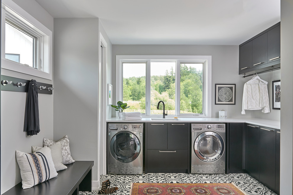 Idee per una lavanderia design con lavello sottopiano, ante lisce, ante grigie, pareti grigie, lavatrice e asciugatrice affiancate, pavimento multicolore e top bianco