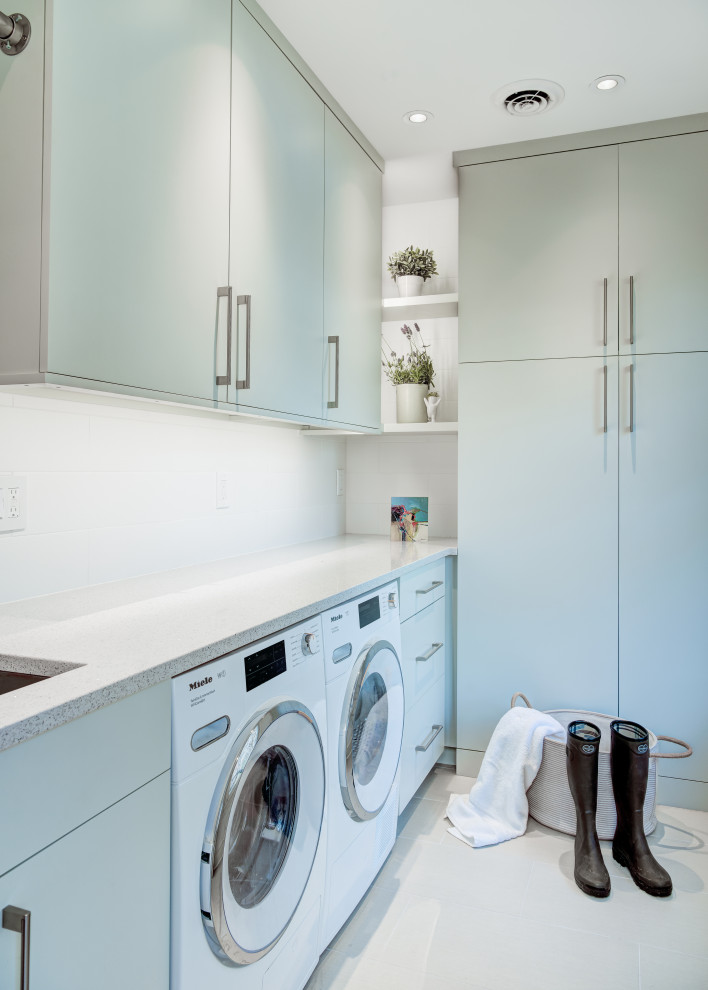 Modern inredning av en mellanstor vita l-formad vitt tvättstuga enbart för tvätt och med garderob, med en undermonterad diskho, släta luckor, gröna skåp, bänkskiva i kvarts, gröna väggar och mellanmörkt trägolv