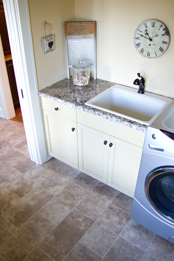 Bild på en mellanstor rustik linjär tvättstuga enbart för tvätt, med en nedsänkt diskho, vita skåp, granitbänkskiva, beige väggar, skiffergolv, en tvättmaskin och torktumlare bredvid varandra och luckor med infälld panel