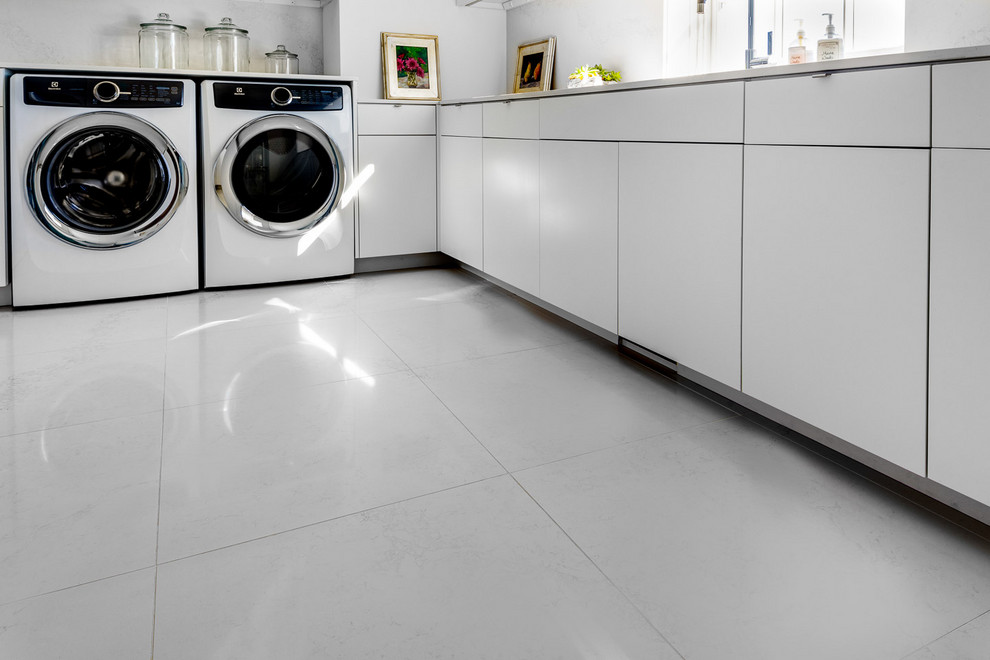 Inredning av en modern stor vita l-formad vitt tvättstuga enbart för tvätt, med en undermonterad diskho, bänkskiva i kvarts, en tvättmaskin och torktumlare bredvid varandra och vitt golv