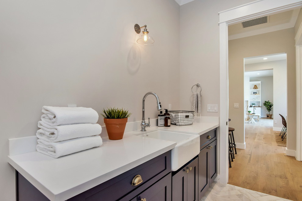 Example of a mid-sized arts and crafts single-wall marble floor and white floor dedicated laundry room design in Phoenix with a farmhouse sink, shaker cabinets, blue cabinets, quartzite countertops, gray walls, a side-by-side washer/dryer and white countertops