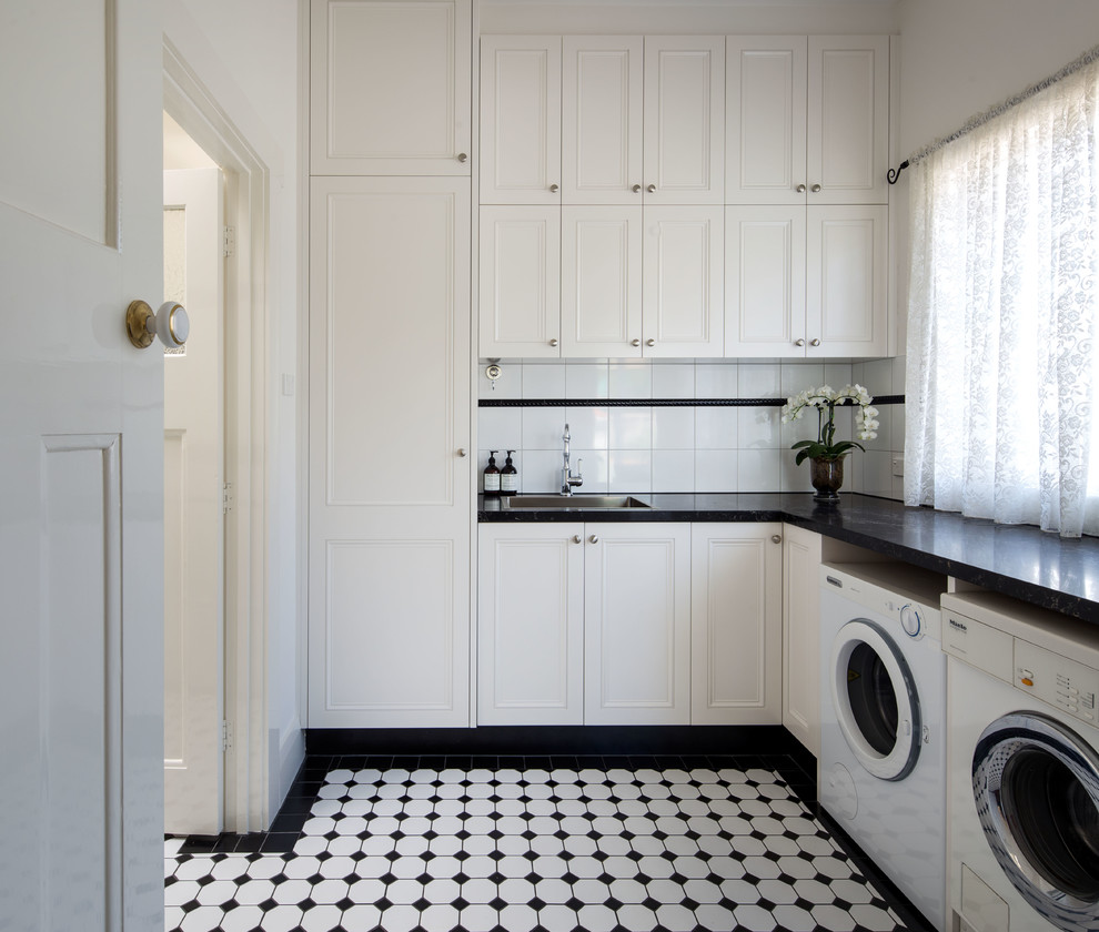 Mid-sized elegant l-shaped ceramic tile and white floor dedicated laundry room photo in Melbourne with a drop-in sink, shaker cabinets, white cabinets, granite countertops, white walls and a side-by-side washer/dryer