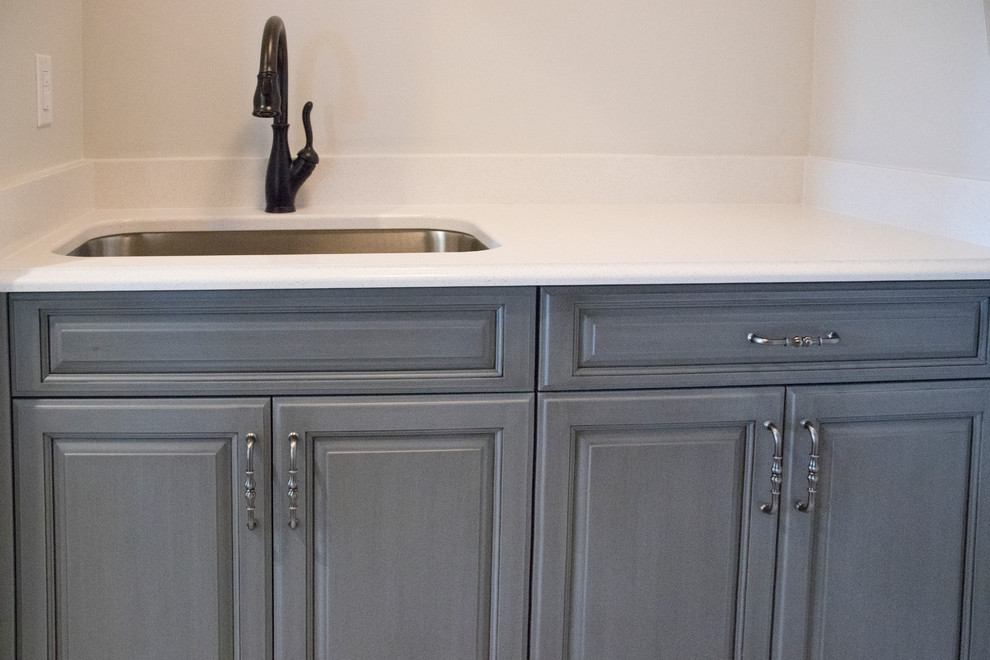 Exempel på en mellanstor klassisk parallell tvättstuga enbart för tvätt, med en undermonterad diskho, luckor med upphöjd panel, grå skåp, bänkskiva i kvarts, grå väggar, klinkergolv i keramik, en tvättmaskin och torktumlare bredvid varandra och grått golv