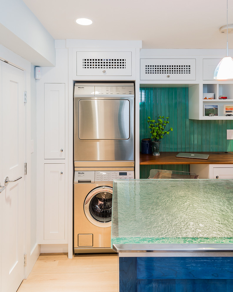 Mittelgroße Klassische Waschküche mit weißen Schränken, Glas-Arbeitsplatte, grüner Wandfarbe, hellem Holzboden, Waschmaschine und Trockner gestapelt, Schrankfronten im Shaker-Stil und türkiser Arbeitsplatte in Boston