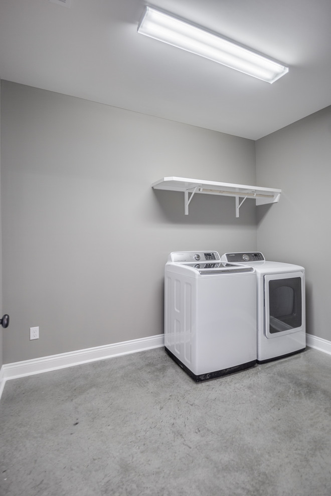 Inspiration för mellanstora klassiska linjära tvättstugor enbart för tvätt, med grå väggar, betonggolv, en tvättmaskin och torktumlare bredvid varandra och grått golv