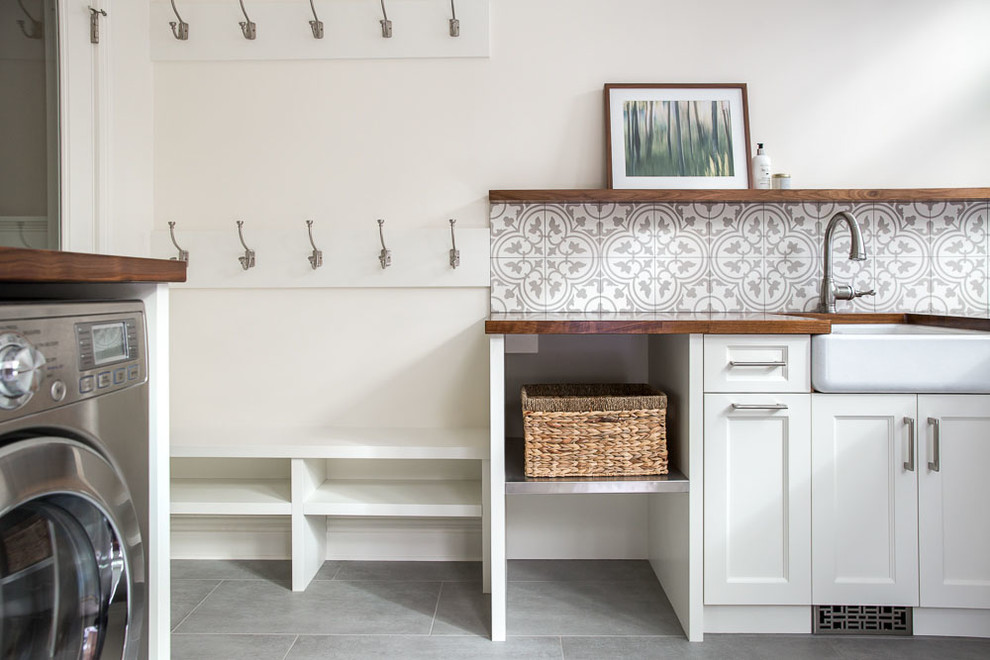 Exempel på en stor klassisk tvättstuga enbart för tvätt, med en rustik diskho, luckor med infälld panel, vita skåp, träbänkskiva, vita väggar, klinkergolv i porslin, en tvättmaskin och torktumlare bredvid varandra och grått golv