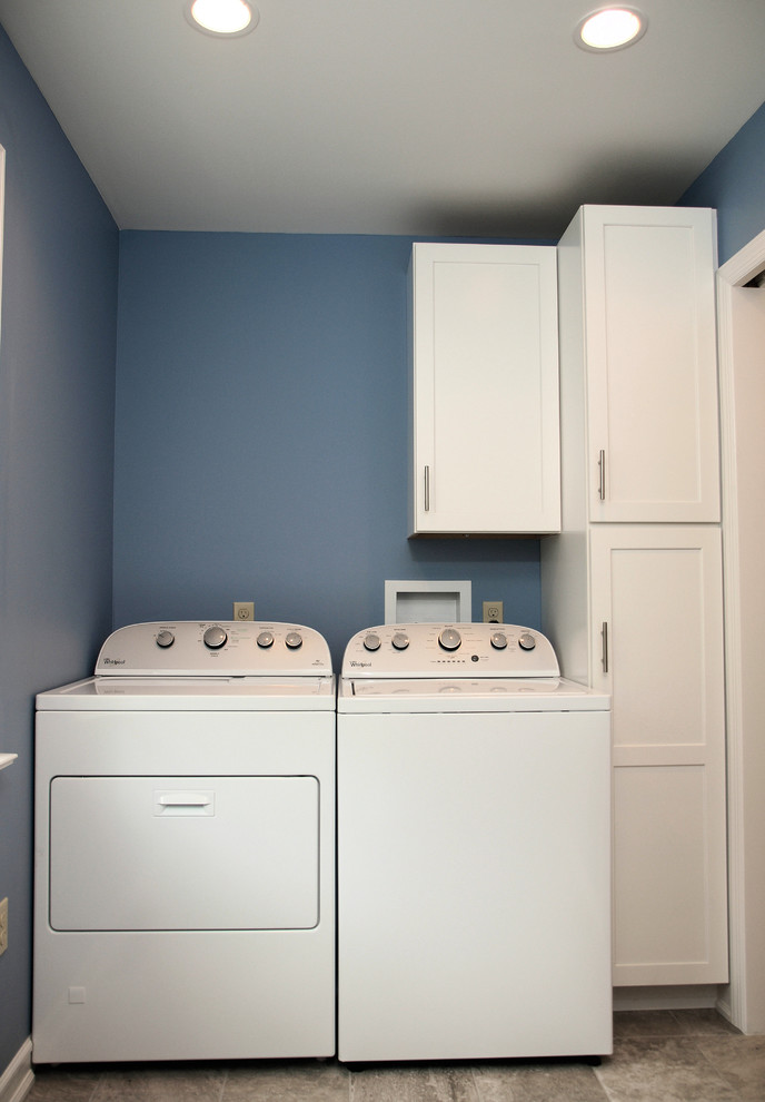 Ejemplo de cuarto de lavado lineal clásico de tamaño medio con armarios estilo shaker, puertas de armario blancas, paredes azules, suelo de baldosas de porcelana y lavadora y secadora juntas