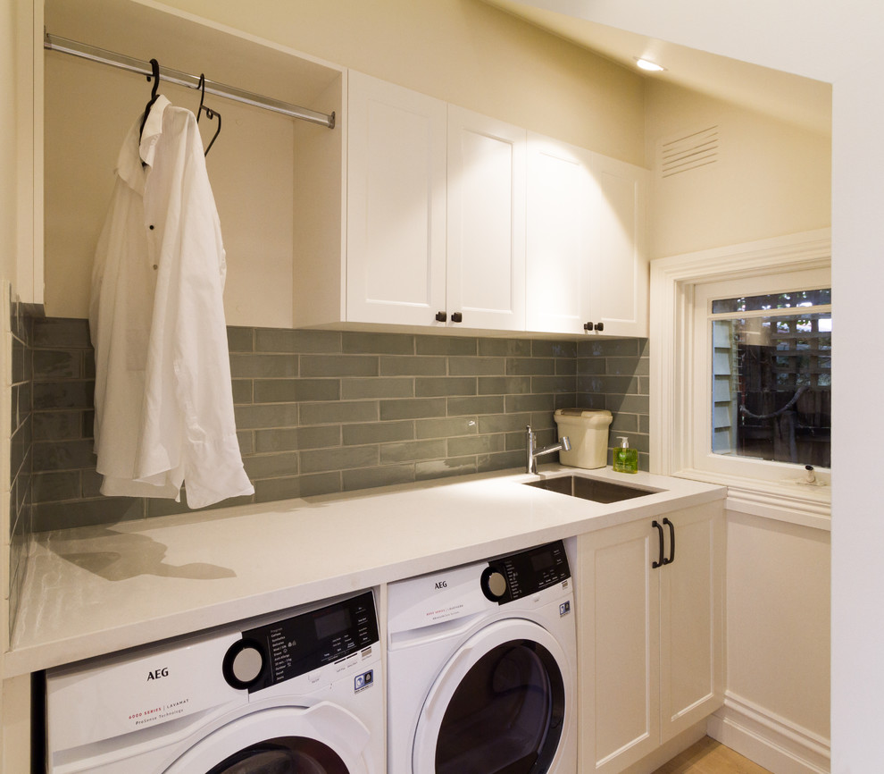 Idéer för att renovera en liten vintage vita parallell vitt tvättstuga enbart för tvätt, med en undermonterad diskho, skåp i shakerstil, vita skåp, bänkskiva i kvarts, vita väggar, ljust trägolv, en tvättmaskin och torktumlare bredvid varandra och beiget golv