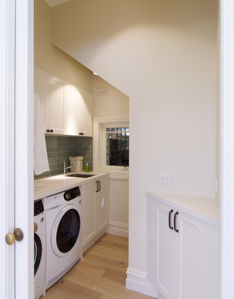 Small classic galley separated utility room in Melbourne with a submerged sink, shaker cabinets, white cabinets, engineered stone countertops, white walls, light hardwood flooring, a side by side washer and dryer, beige floors and white worktops.