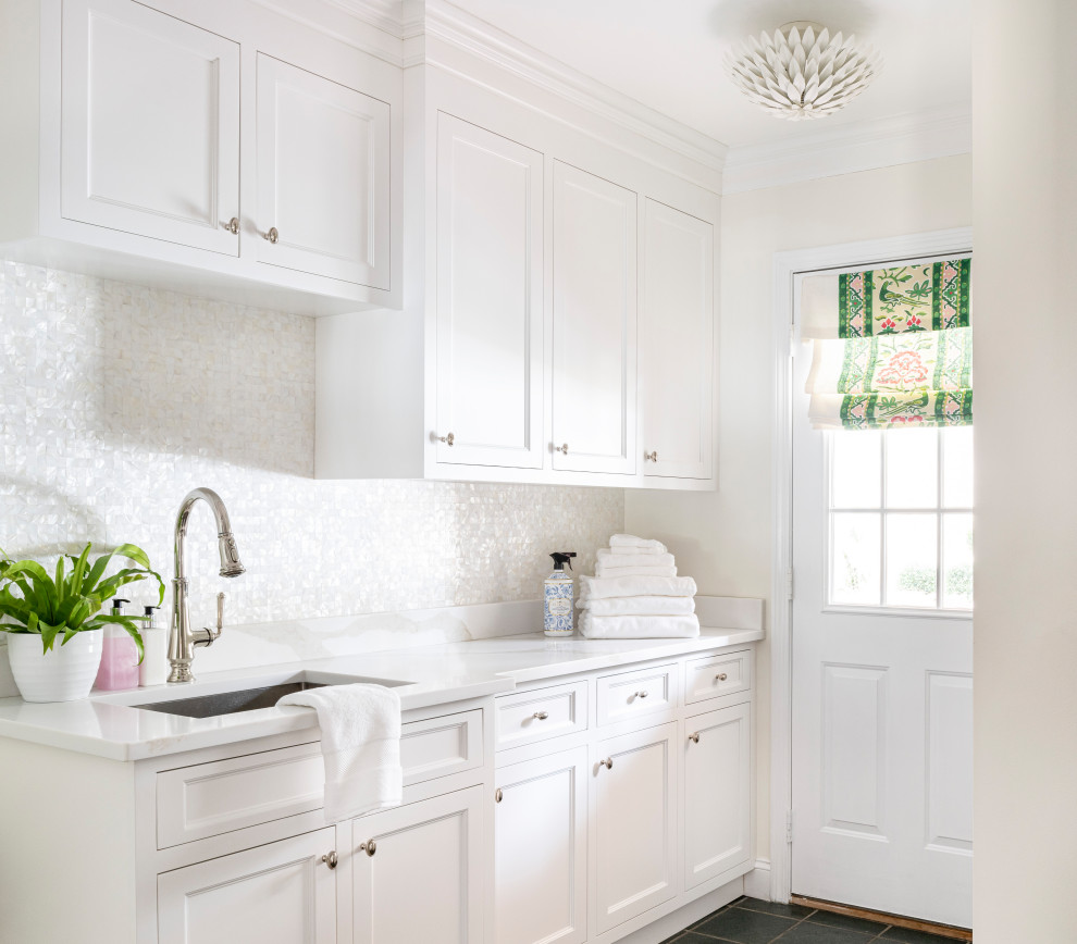 Modelo de cuarto de lavado lineal clásico renovado de tamaño medio con puertas de armario blancas, encimera de cuarzo compacto, salpicadero con mosaicos de azulejos, paredes blancas, suelo de baldosas de cerámica y encimeras blancas