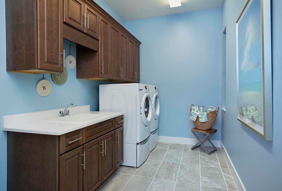Foto de cuarto de lavado lineal marinero de tamaño medio con fregadero encastrado, armarios con paneles con relieve, puertas de armario de madera en tonos medios, paredes azules, lavadora y secadora juntas y suelo gris