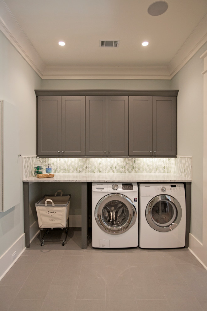 Inredning av en klassisk stor parallell tvättstuga enbart för tvätt, med skåp i shakerstil, marmorbänkskiva, grå väggar, klinkergolv i porslin, en tvättmaskin och torktumlare bredvid varandra och grå skåp
