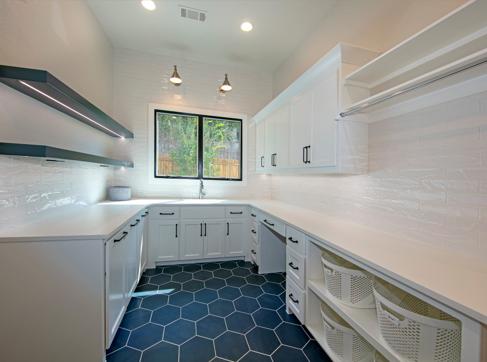 ダラスにある高級な広いトランジショナルスタイルのおしゃれな洗濯室 (ll型、アンダーカウンターシンク、シェーカースタイル扉のキャビネット、白いキャビネット、クオーツストーンカウンター、白いキッチンパネル、セメントタイルのキッチンパネル、白い壁、セラミックタイルの床、左右配置の洗濯機・乾燥機、青い床、白いキッチンカウンター) の写真