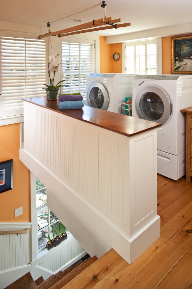 ボストンにあるお手頃価格の小さなトランジショナルスタイルのおしゃれな家事室 (ll型、白いキャビネット、木材カウンター、オレンジの壁、左右配置の洗濯機・乾燥機) の写真
