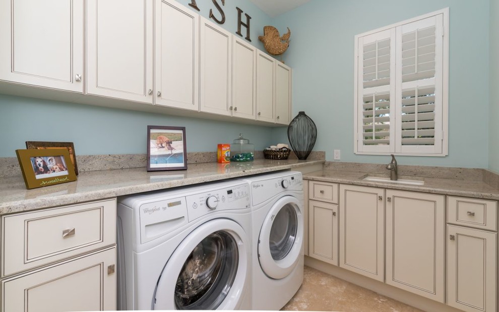 Idéer för att renovera en mellanstor vintage l-formad tvättstuga enbart för tvätt, med en undermonterad diskho, luckor med upphöjd panel, vita skåp, granitbänkskiva, blå väggar, travertin golv och en tvättmaskin och torktumlare bredvid varandra
