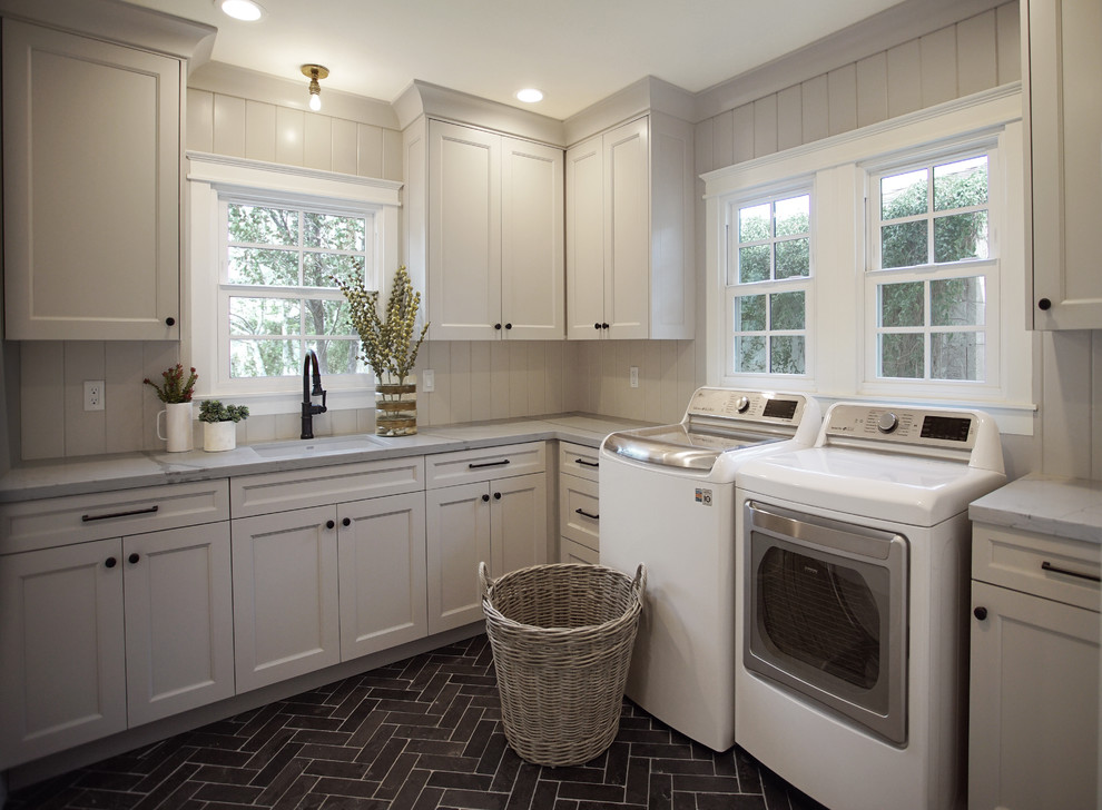 Idéer för en mellanstor klassisk grå l-formad tvättstuga enbart för tvätt, med en undermonterad diskho, skåp i shakerstil, grå skåp, bänkskiva i kvarts, grått stänkskydd, stänkskydd i trä, vita väggar, kalkstensgolv, en tvättmaskin och torktumlare bredvid varandra och svart golv