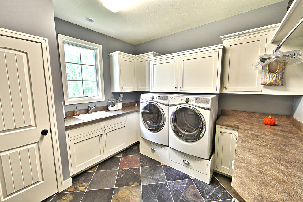 Immagine di una sala lavanderia classica con lavello da incasso, ante bianche, top in laminato, pareti blu, pavimento in ardesia e lavatrice e asciugatrice affiancate