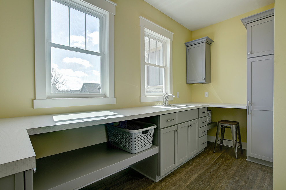 This is an example of a small classic galley separated utility room in Grand Rapids with a built-in sink, shaker cabinets, grey cabinets, laminate countertops, yellow walls, medium hardwood flooring, a side by side washer and dryer and brown floors.