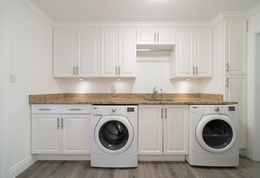 Inspiration för mellanstora klassiska linjära brunt tvättstugor enbart för tvätt, med en undermonterad diskho, granitbänkskiva, vita väggar, mellanmörkt trägolv och grått golv