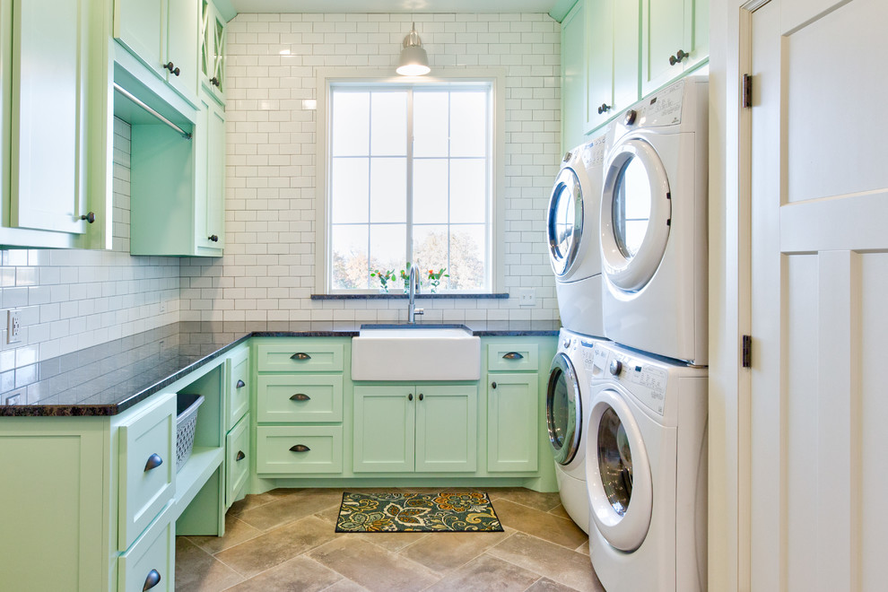 Lantlig inredning av en u-formad tvättstuga enbart för tvätt, med en rustik diskho, skåp i shakerstil, gröna skåp, granitbänkskiva, vita väggar, klinkergolv i keramik, en tvättpelare och grått golv
