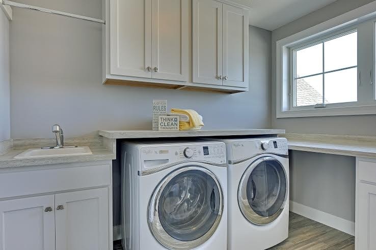 Inspiration för små klassiska linjära grått tvättstugor enbart för tvätt, med en nedsänkt diskho, skåp i shakerstil, vita skåp, grå väggar, klinkergolv i porslin, en tvättmaskin och torktumlare bredvid varandra och brunt golv