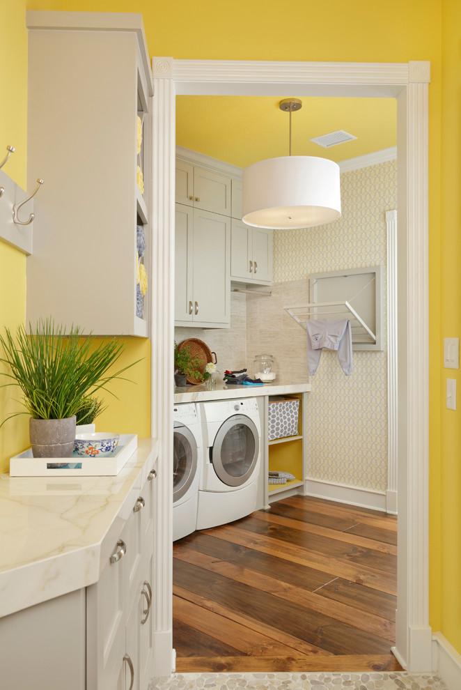 Idee per una piccola sala lavanderia chic con ante in stile shaker, ante grigie, pavimento in legno massello medio, lavatrice e asciugatrice affiancate e pareti gialle