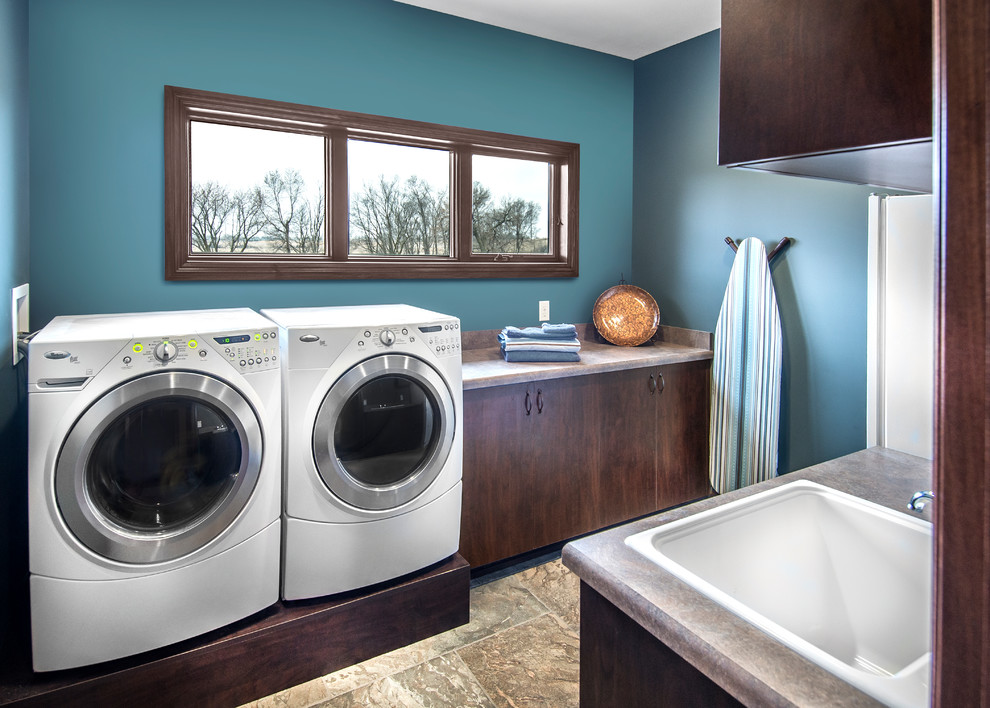 オマハにある高級な中くらいなトランジショナルスタイルのおしゃれな洗濯室 (ll型、ドロップインシンク、フラットパネル扉のキャビネット、濃色木目調キャビネット、ラミネートカウンター、青い壁、クッションフロア、左右配置の洗濯機・乾燥機、茶色い床、茶色いキッチンカウンター) の写真