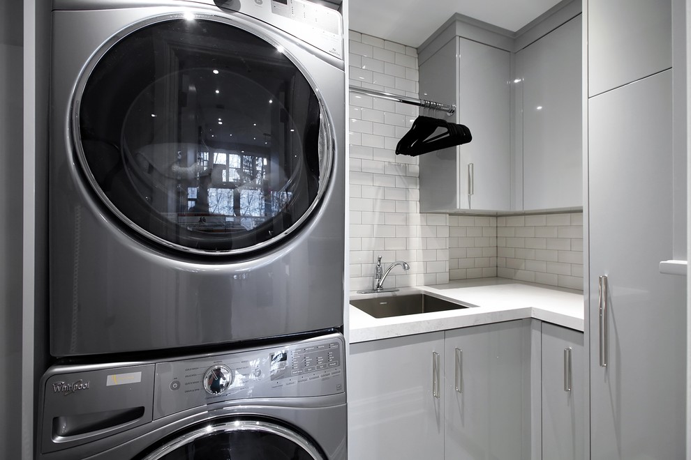 Photo of a medium sized contemporary l-shaped separated utility room in Toronto with a submerged sink, flat-panel cabinets, grey cabinets, laminate countertops, grey walls, porcelain flooring, a stacked washer and dryer and grey floors.