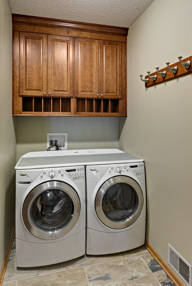 Exempel på en liten klassisk linjär tvättstuga enbart för tvätt, med luckor med upphöjd panel, skåp i mellenmörkt trä, klinkergolv i porslin, en tvättmaskin och torktumlare bredvid varandra, grått golv och grå väggar