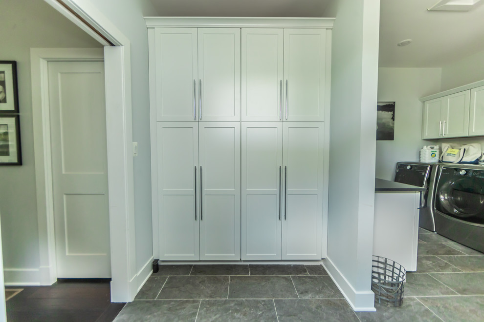 Design ideas for a large classic galley utility room in Baltimore with shaker cabinets, white cabinets, composite countertops, white splashback, ceramic splashback, black worktops, grey walls, porcelain flooring, a side by side washer and dryer and grey floors.
