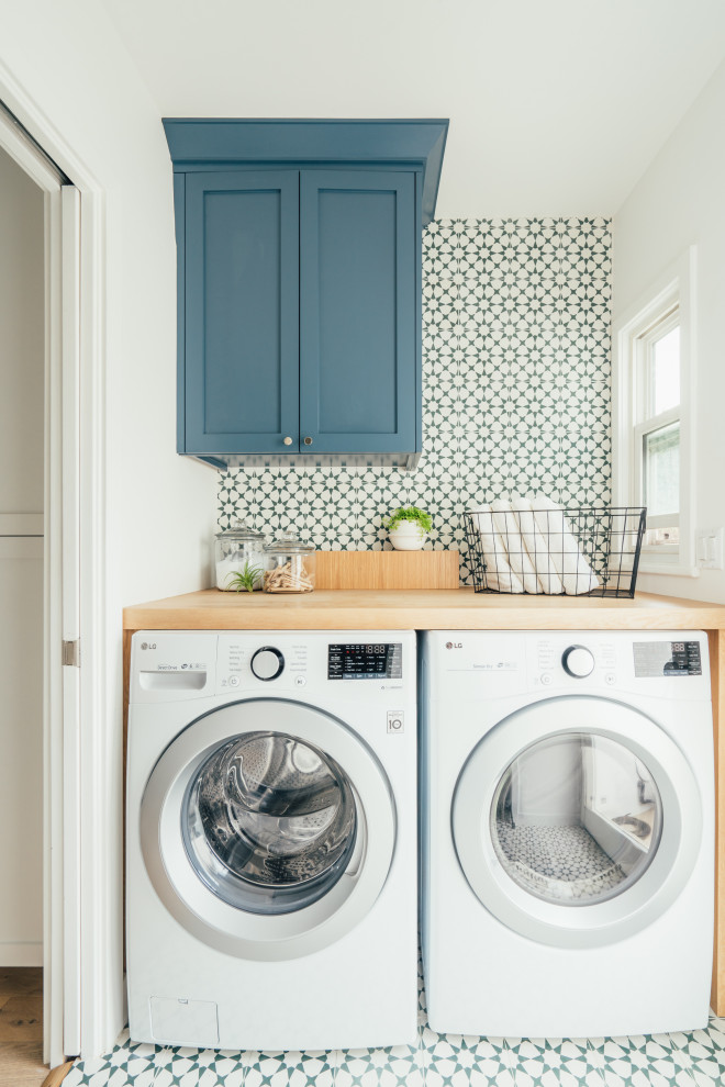 Idee per una sala lavanderia country con ante in stile shaker, ante blu, top in legno, pareti bianche, lavatrice e asciugatrice affiancate, pavimento multicolore e top marrone
