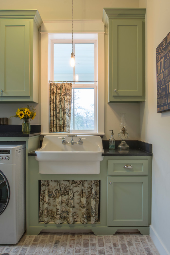 Foto på ett mellanstort lantligt parallellt grovkök, med en rustik diskho, skåp i shakerstil, gröna skåp, granitbänkskiva, vita väggar, tegelgolv och en tvättmaskin och torktumlare bredvid varandra